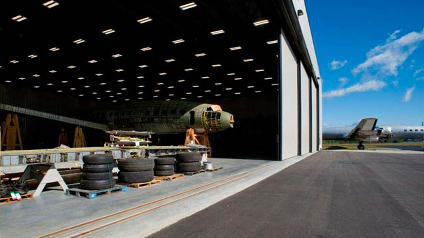 View of an airplane hangar open door with materials stacked towards the front. 