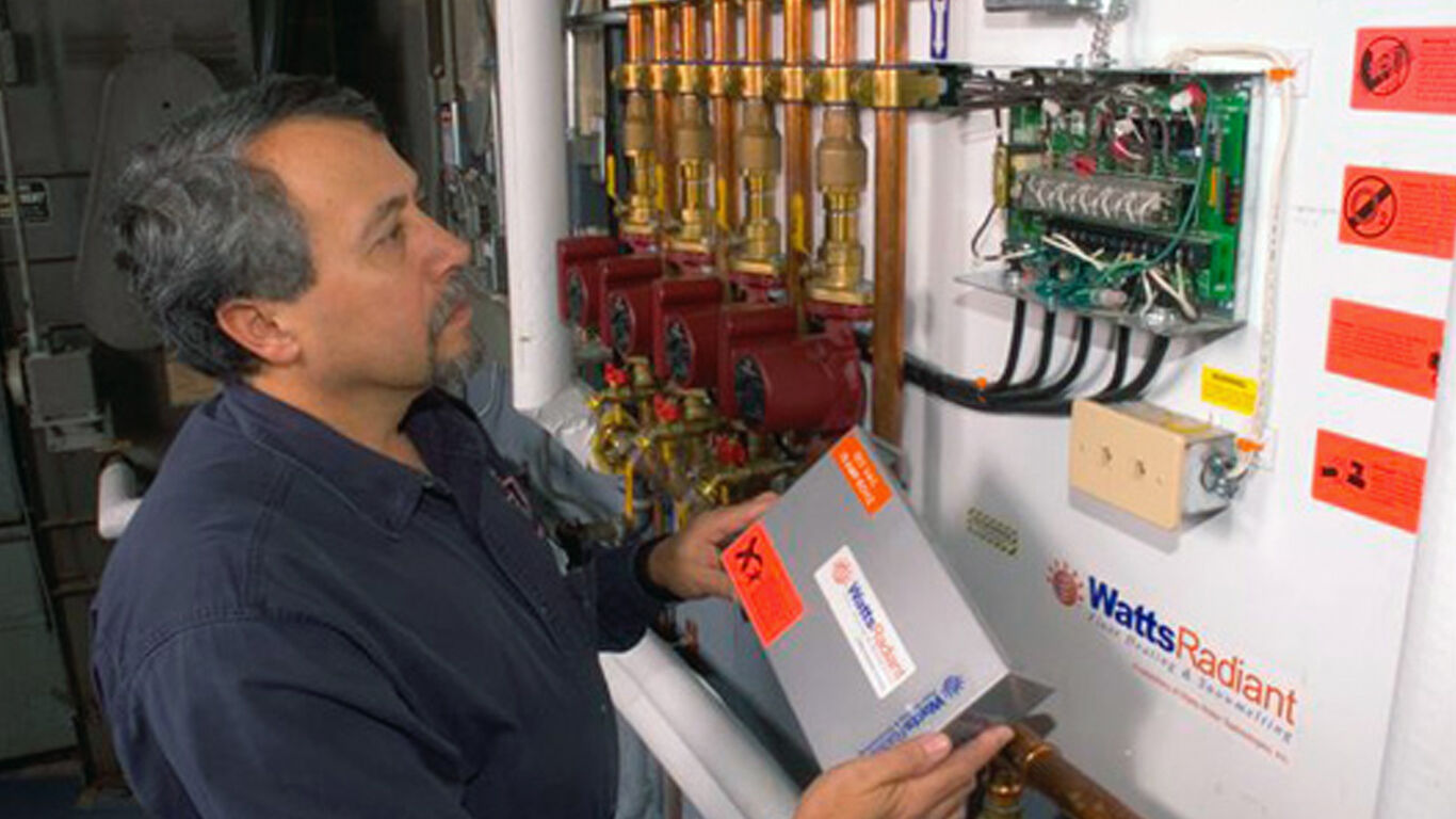 Man working on floor heating system controls. 