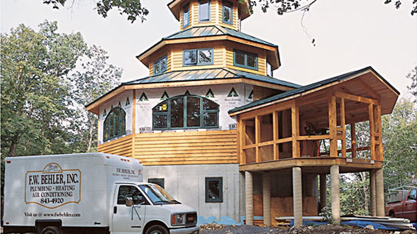 Outside of a lighthouse made of wood with a white workers van parked in front.