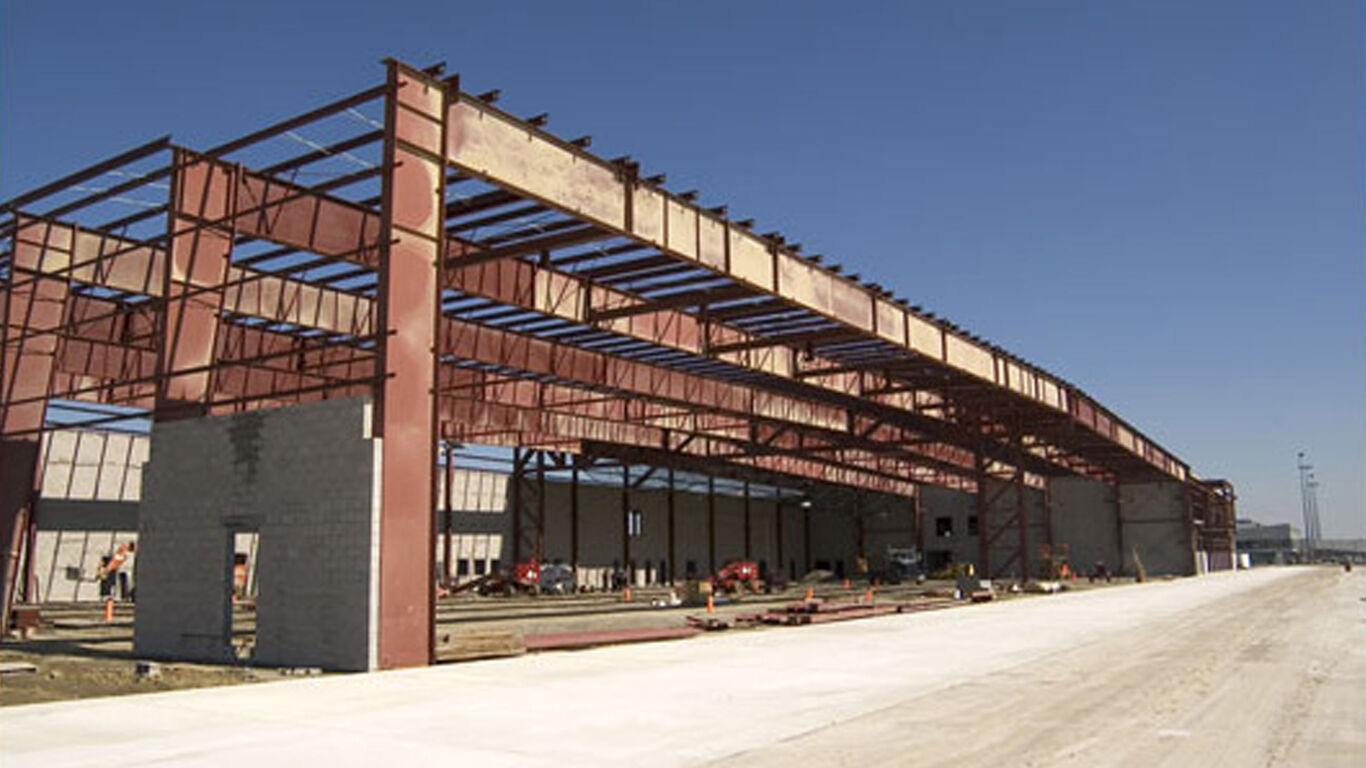 A warehouse being built, it has three of its walls up and the supports for the roof